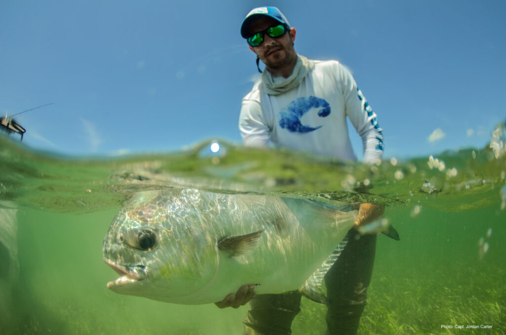 Captain wearing shirt with Costa logo holding permit underwater