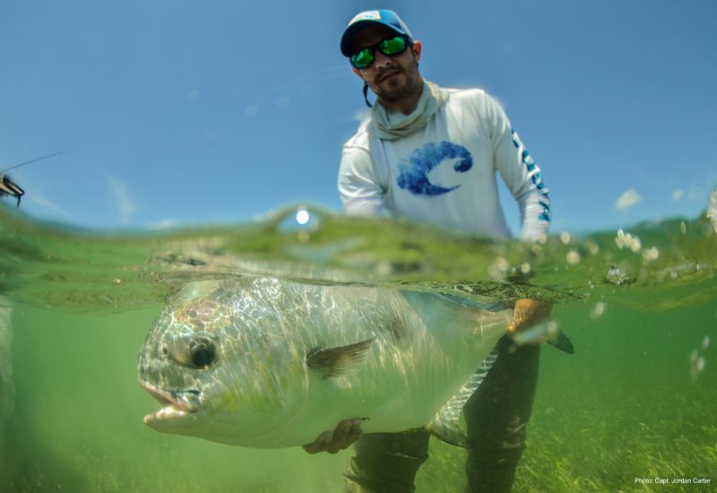 Captain wearing shirt with Costa logo holding permit underwater